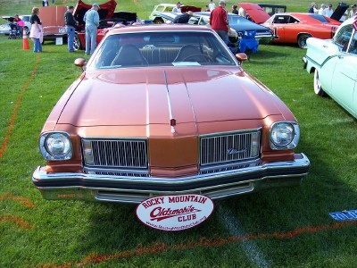 1972 Ford Ranchero - Copper 1973 Oldsmobile Cutlass displayed at an outdoor car show with other vehicles present.
