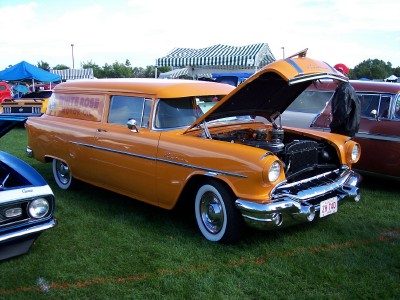 1972 Ford Ranchero - An orange sedan delivery van is parked on grass with its hood open, displaying its engine.