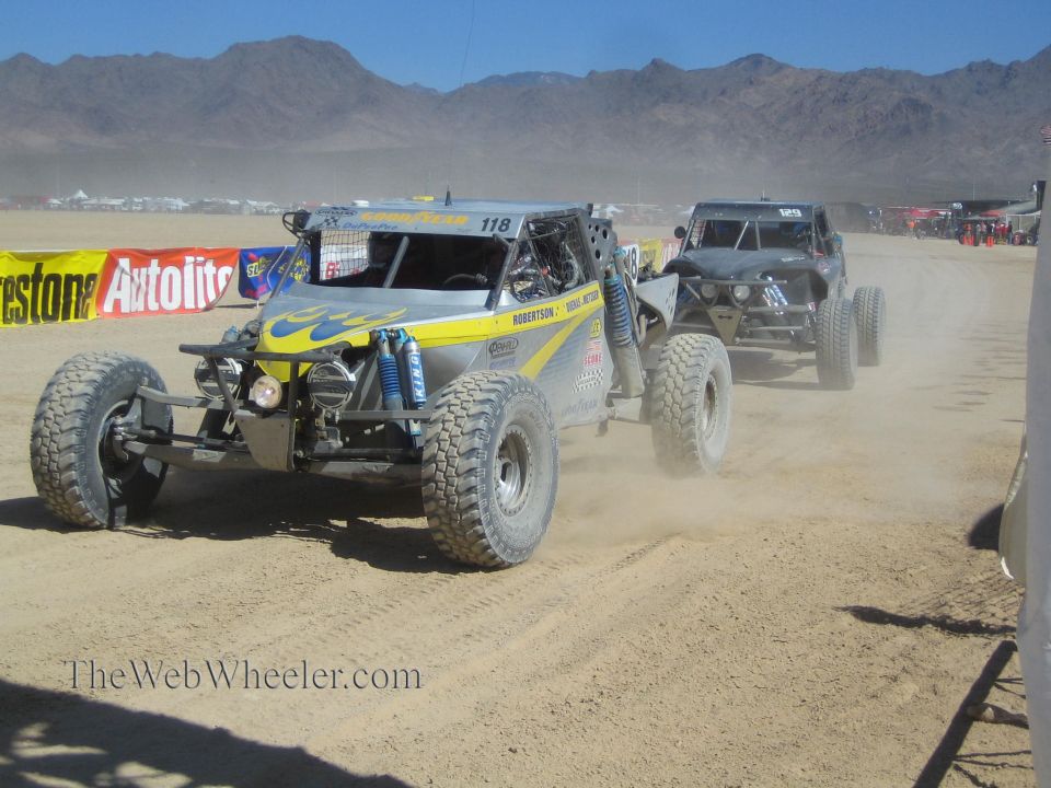 Two off-road race buggies on a sandy desert course, lead buggy #118 yellow and gray