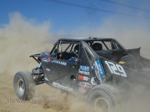1990 Ford Bronco - black off-road race buggy numbered 129 with Jangaard and BFGoodrich livery throws up heavy dust on a desert course.