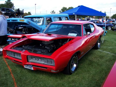 1972 Ford Ranchero - A red 1969 Pontiac GTO is displayed with its hood open at an outdoor car show, with other vehicles visible.