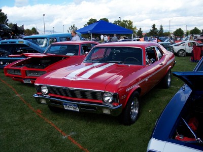 1972 Ford Ranchero - A red coupe with white racing stripes is parked on a grassy field at an outdoor car show.
