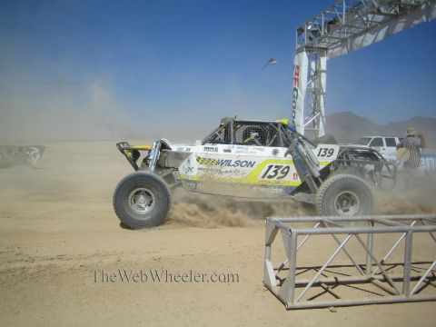 1990 Ford Bronco - white and yellow off-road race buggy numbered 139 with Wilson livery launches from a dusty desert start line.