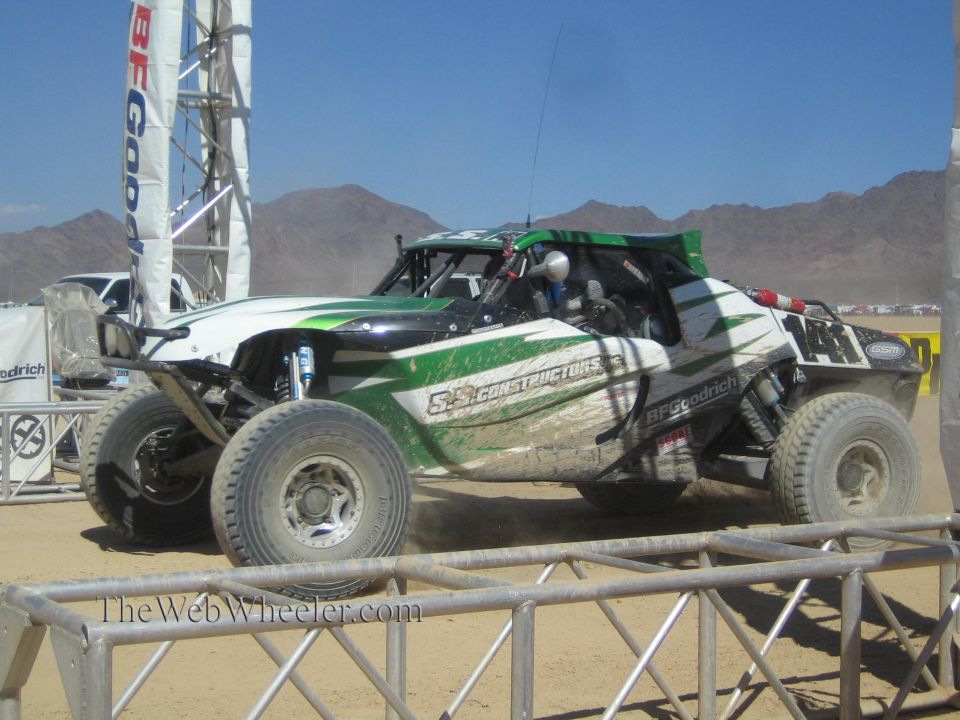 Green and white off-road race buggy with construction livery on desert course