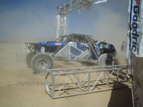 1990 Ford Bronco - blue off-road race buggy numbered 200 with McMillin Homes livery kicks up heavy dust at a desert start arch.