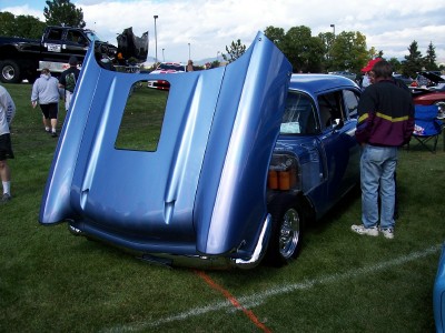 1972 Ford Ranchero - A blue sedan is displayed with its hood open, revealing the engine compartment to onlookers at an outdoor event.