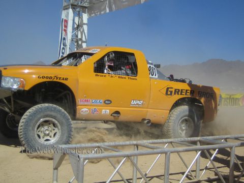 1990 Ford Bronco - orange off-road race truck numbered 801 with Greer Bros and Goodyear livery races over a desert course kicking up sand.