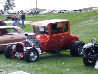1972 Ford Ranchero - A custom red hot rod coupe with flame decals and a prominent V8 engine is displayed at an outdoor car show.