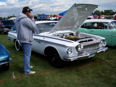 1972 Ford Ranchero - A man talks on his phone next to a white 1961 Plymouth Valiant at an outdoor car show.