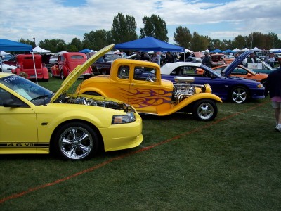 1972 Ford Ranchero - A bright yellow hot rod with flame decals and an exposed engine is displayed at an outdoor car show.