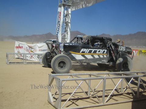 1990 Ford Bronco - black off-road race buggy numbered 135 with Pitton livery races from a desert start line beneath a BFGoodrich arch.