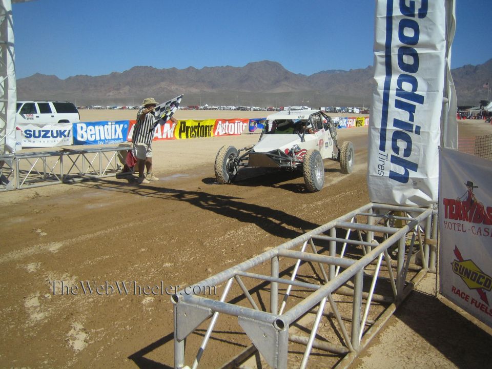 White off-road race buggy approaching finish arch as flagman signals on desert course