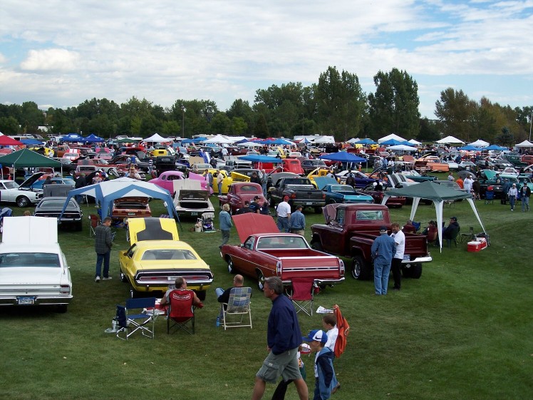 Outdoor car show with rows of cars and tents under a cloudy sky