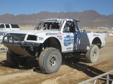 1990 Ford Bronco - white number 701 off-road race truck with BFGoodrich and Factory Racing decals sits on a dirt course.