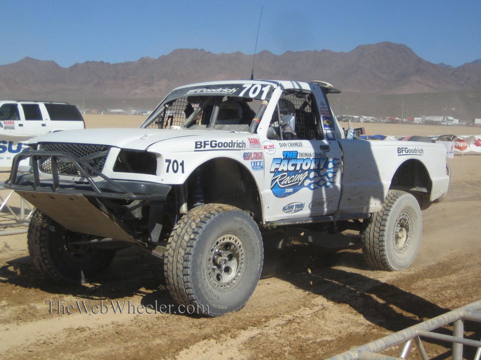 White No. 701 off-road race truck on dirt course with desert mountains behind