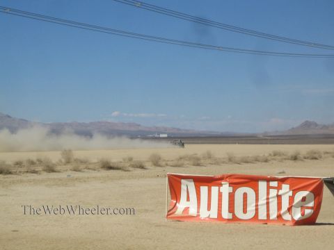 1990 Ford Bronco - distant vehicle kicks up a dust trail across a flat desert while a large orange Autolite banner stands in the foreground.