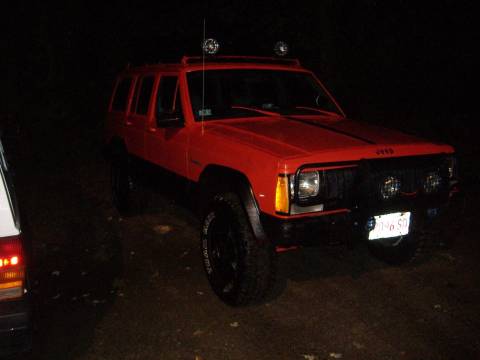 Red 1990 Jeep Cherokee with aftermarket grille and lights, parked at night