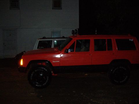 1990 Jeep Cherokee - A red 1990 Jeep Cherokee is parked next to another SUV at night.