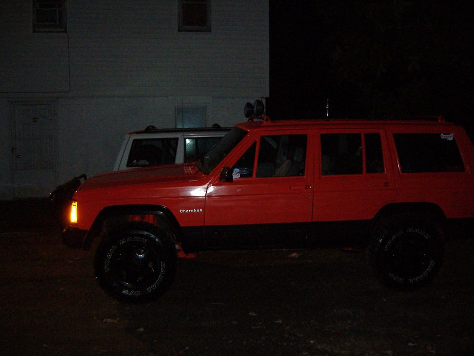 Red 1990 Jeep Cherokee side view with black trim and roof lights