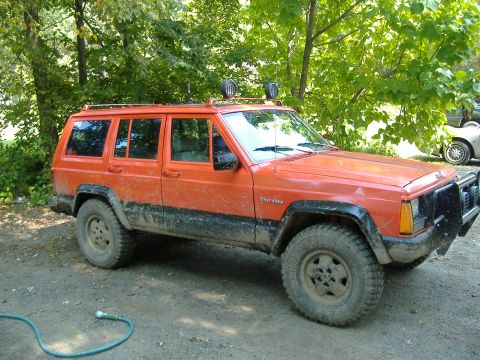 1990 Jeep Cherokee - This orange 1990 Jeep Cherokee features a roof rack and auxiliary lights, suggesting it's equipped for off-road adventures.