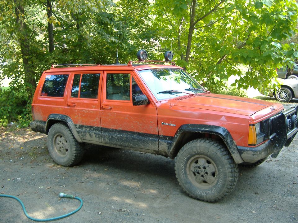 Orange 1990 Jeep Cherokee with roof rack and off-road lights parked outdoors