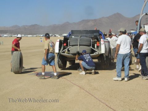 1990 Ford Bronco - Pit crew members gather and work at the rear of a number 17 off-road race truck in a dusty desert pit.