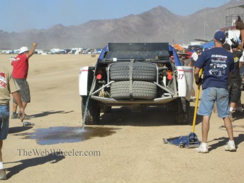 1990 Ford Bronco - Crew members service the rear of a number 17 off-road race truck loaded with spare tires in a dusty desert pit.