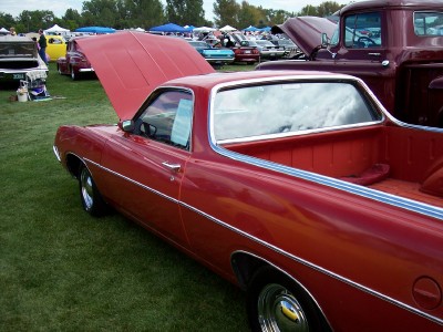 1972 Ford Ranchero - A red pickup truck is displayed with its hood up at an outdoor event, with other vehicles in the background.
