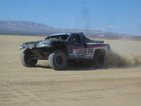 1990 Ford Bronco - dark Lucas Oil number 17 off-road race truck races across a desert course throwing up a large dust cloud.