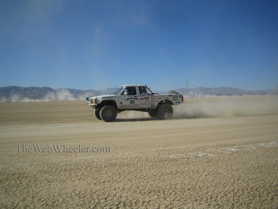 White off-road race truck speeding across desert leaving long dust trail