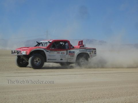 1990 Ford Bronco - red and white number 4 off-road race truck races across a desert course, throwing up a cloud of dust.