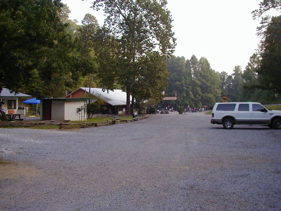 White SUV parked on gravel lot with trees and buildings in background