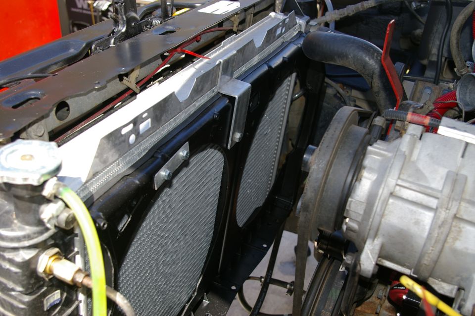 Close-up of a vehicle's radiator and dual electric fans, with hoses and engine components visible