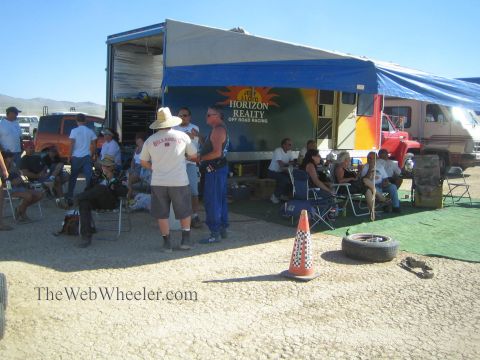 1990 Ford Bronco - crowd relaxes under a Horizon Realty Off Road Racing canopy at a dusty desert pit area with spare tires nearby.