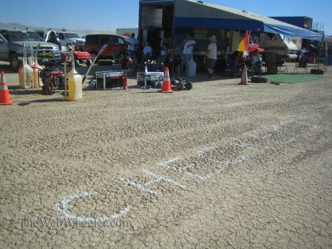 1990 Ford Bronco - desert pit scene with fuel jugs and cones, the word Checkers chalked across the cracked lakebed in front of a canopy.