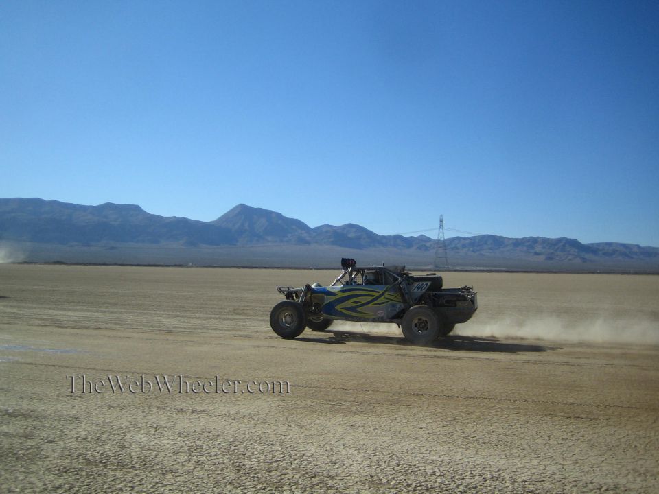 Blue and green off-road race buggy racing across desert flat with mountains behind