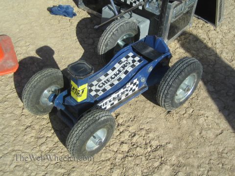 1990 Ford Bronco - small blue four-wheeled ride-on pit cart decorated with checkered-flag graphics sits on the cracked desert ground.