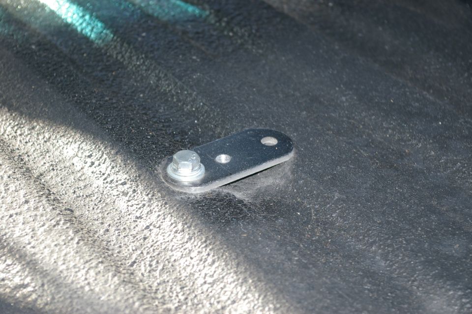 Metal bracket with a single bolt attached to a dark, textured surface