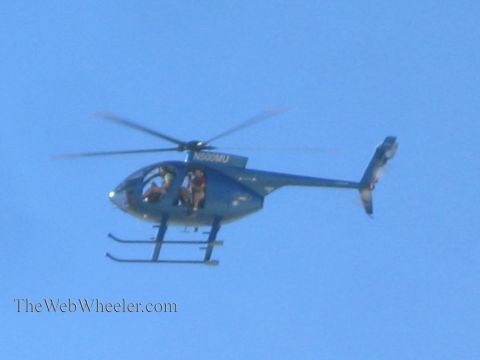 1990 Ford Bronco - blue helicopter registered N500MU flies overhead against a clear sky with people visible in the open side doorway.