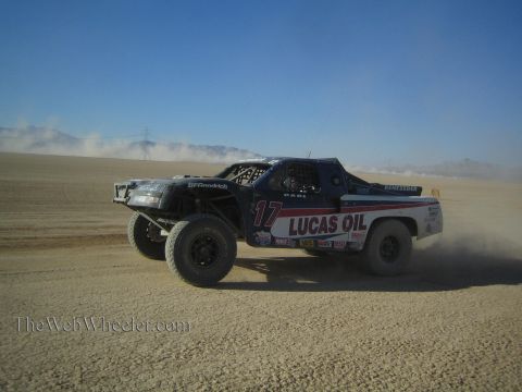 1990 Ford Bronco - dark blue off-road race truck number 17 lettered Lucas Oil speeds across a dusty desert flat.