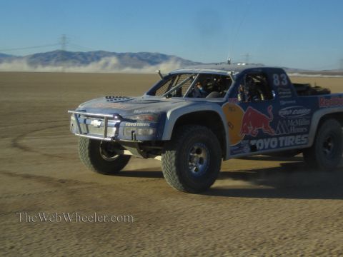 1990 Ford Bronco - silver off-road race truck number 83 with Red Bull and Toyo Tires livery races across a dusty desert flat.