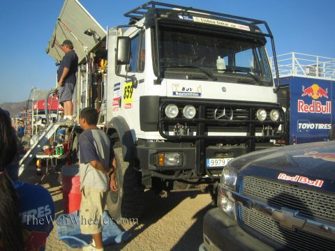 1990 Ford Bronco - white Mercedes-Benz support truck number 559 parks beside a Red Bull Chevrolet pickup at a busy desert race pit.
