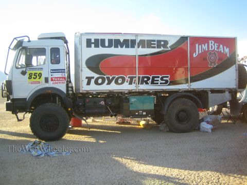 1990 Ford Bronco - white heavy-duty Mercedes-Benz race support truck numbered 859 sits in a desert pit, its box body wrapped in Hummer, Jim Beam, and Toyo Tir…