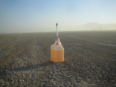 1990 Ford Bronco - white plastic jug filled with orange fluid and capped with a slim antenna sits alone on a hazy, cracked desert lakebed.