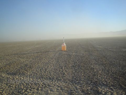 1990 Ford Bronco - lone white jug of orange fluid with a thin antenna marks a spot on a wide, cracked desert lakebed under a hazy sky.
