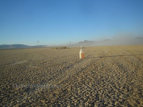 1990 Ford Bronco - white jug of orange liquid topped with an antenna sits on a cracked desert lakebed, with power-line towers and mountains in the distant haz…