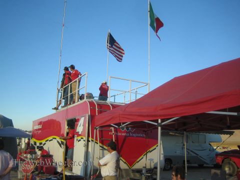 1990 Ford Bronco - Crew stand on the elevated deck of a red Mexicana Logistics #4 race trailer flying US and Mexican flags, with a canopy and motorhome alongs…
