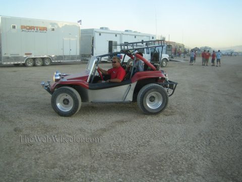 1990 Ford Bronco - man drives a red-and-silver open dune buggy across a desert lot past large Porter Racing enclosed trailers.