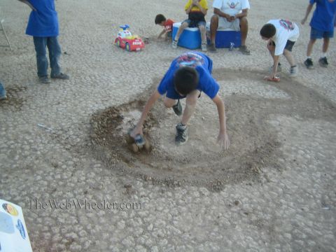 1990 Ford Bronco - boy in a blue shirt digs a hole in the dirt with a toy truck while other children play with toy cars at a desert race camp.