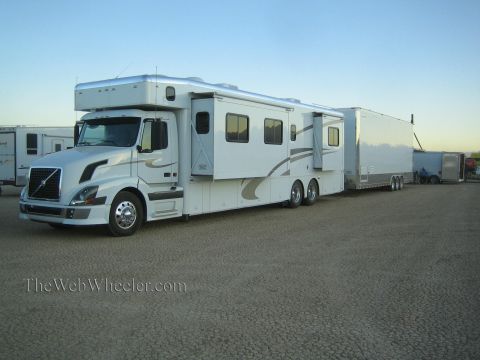 1990 Ford Bronco - large white Volvo truck-based motorhome with a slide-out tows a long enclosed trailer in a dirt lot among other race haulers.